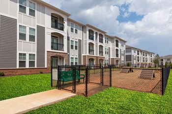 a fenced in dog park in front of an apartment building